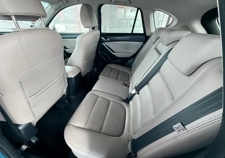 Vue intérieure arrière montrant les sièges en cuir beige du Mazda CX-5 bleu, avec ceintures de sécurité visibles.