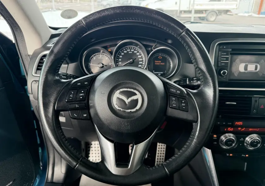 Vue intérieure centrée sur le volant en cuir noir du Mazda CX-5 bleu 2013 avec tableau de bord et écran multimédia visible.