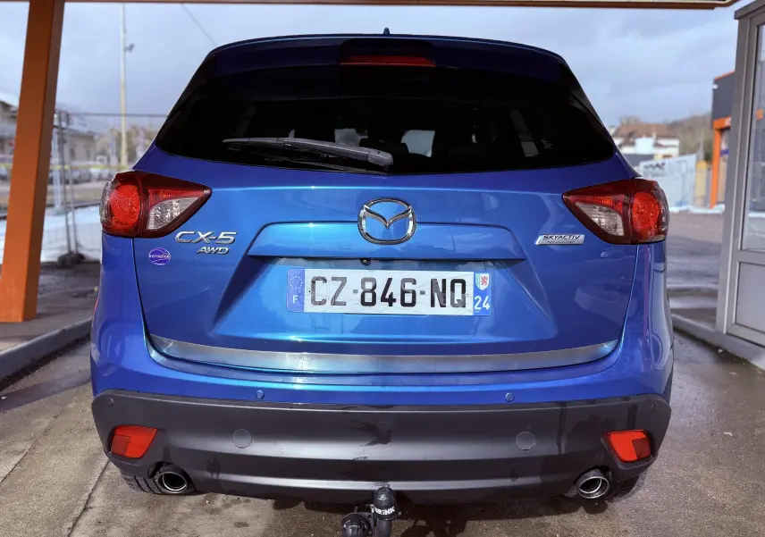 Vue arrière d'un Mazda CX-5 bleu 2013 avec logo Mazda, plaques françaises et attelage de remorque visible.