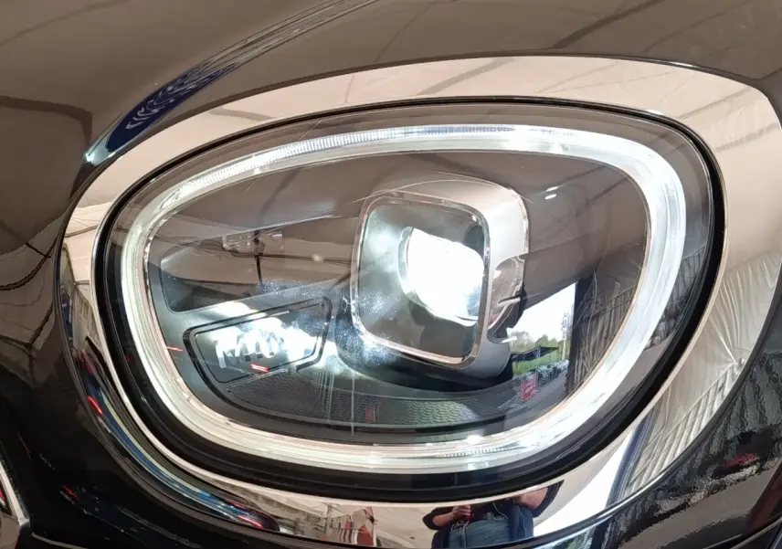 Gros plan sur le phare avant droit LED d’un MINI Countryman Cooper SE noir, soulignant le contour chromé et la signature lumineuse distinctive.