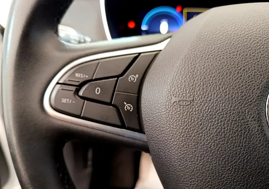 Gros plan sur les commandes du régulateur de vitesse au volant noir d’une Renault Mégane Business E-Tech hybride rechargeable blanche.