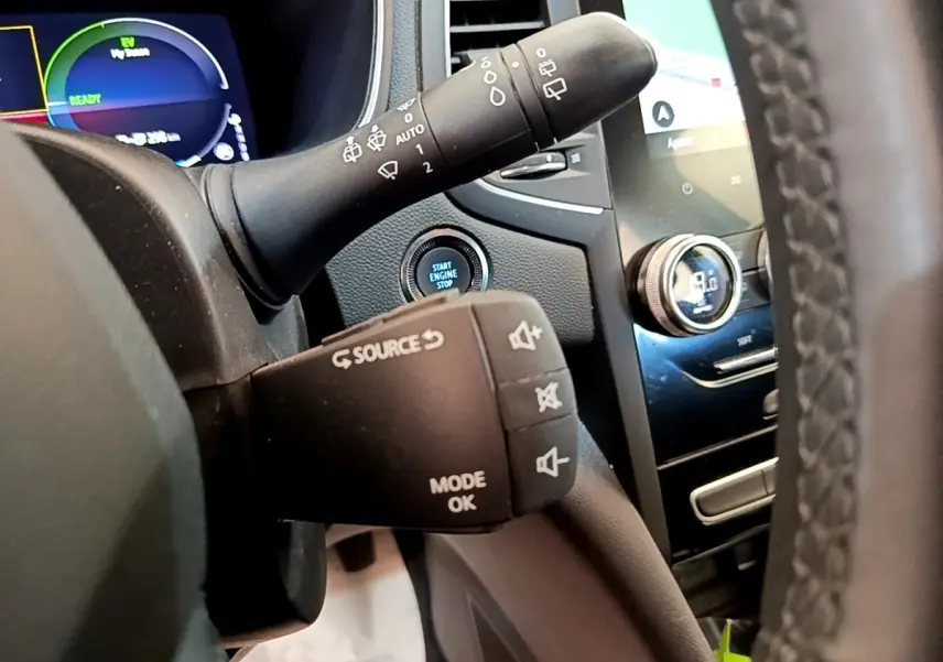 Gros plan sur la commande au volant et le tableau de bord digital de la Renault Mégane Business E-Tech hybride blanche, intérieur avant.