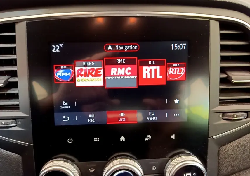 Écran tactile central affichant la navigation et stations radio dans l’habitacle d’une Renault Mégane Business E-Tech hybride blanche.