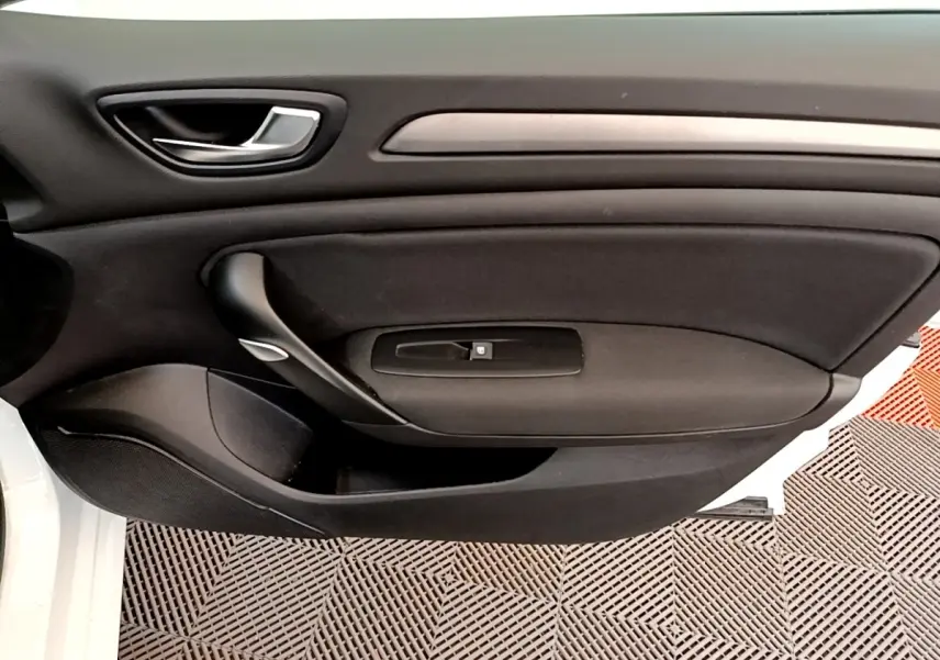 Vue rapprochée de la porte intérieure côté conducteur d’une Renault Mégane Business E-Tech blanche, avec poignée noire et bouton de vitre.