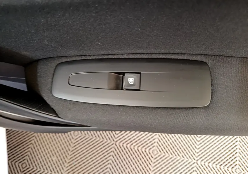 Gros plan sur le bouton de commande de la vitre électrique côté conducteur dans une Renault Mégane blanche hybride rechargeable.