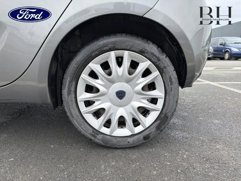 Gros plan sur la roue arrière droite grise argentée d'une Lancia Ypsilon 2014 avec enjoliveur argenté et logo central bleu.
