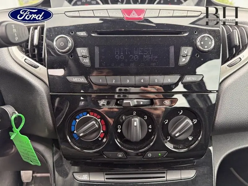 Vue rapprochée du tableau de bord noir brillant de la Lancia Ypsilon gris Argento, mettant en valeur les commandes de climatisation et radio.