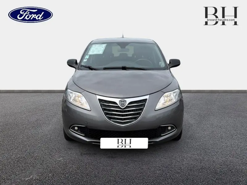 Vue de face d'une Lancia Ypsilon gris Argento 2014 avec calandre chromée et phares halogènes allumés.