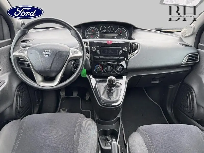 Vue intérieure avant de la Lancia Ypsilon 2014, tableau de bord noir avec volant cuir et levier de vitesses manuel.