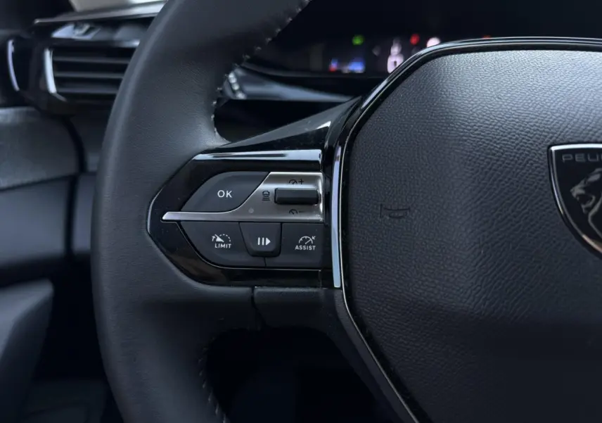 Gros plan sur la partie gauche du volant noir de la Peugeot 308 Hybrid avec commandes de régulateur et assistant de conduite.