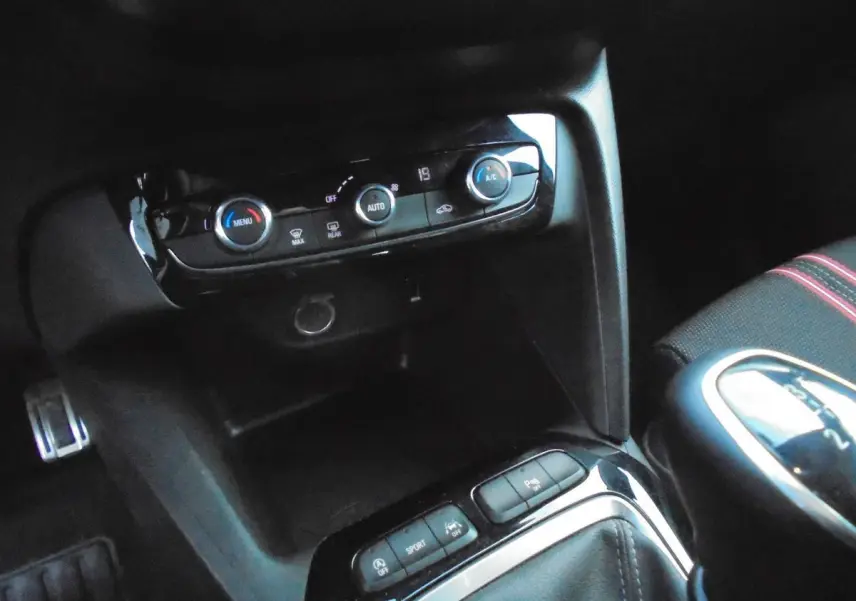 Gros plan sur la console centrale et commandes climatisation d'une Opel Corsa gris quartz, intérieur noir avec surpiqûres rouges.