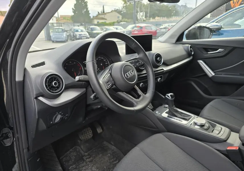 Vue intérieure côté conducteur de l'Audi Q2 2023 noir mythic, avec volant cuir multifonction et console centrale moderne.