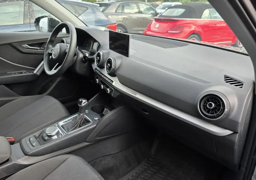 Intérieur avant gauche de l'Audi Q2 35 TFSI 2023 avec tableau de bord noir, écran central et volant multifonction cuir.
