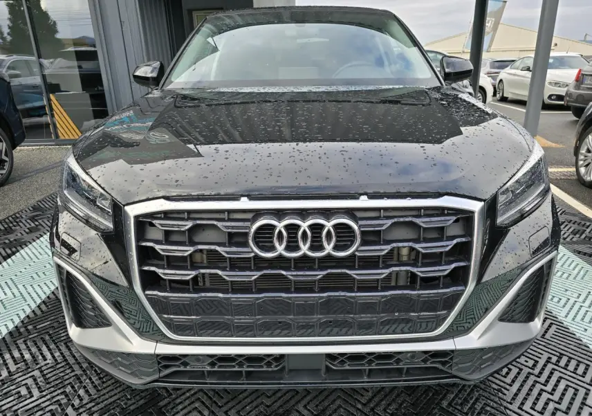 Vue frontale d'un Audi Q2 noir mythic avec calandre large et phares LED sous la pluie.