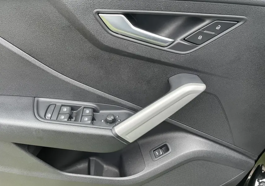 Détail de la porte avant gauche de l'Audi Q2 noir mythic, avec commandes de vitres et poignée argentée.