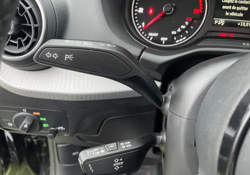 Gros plan sur les commandes au volant d’un Audi Q2 2023 noir mythic, avec levier clignotant et régulateur de vitesse.