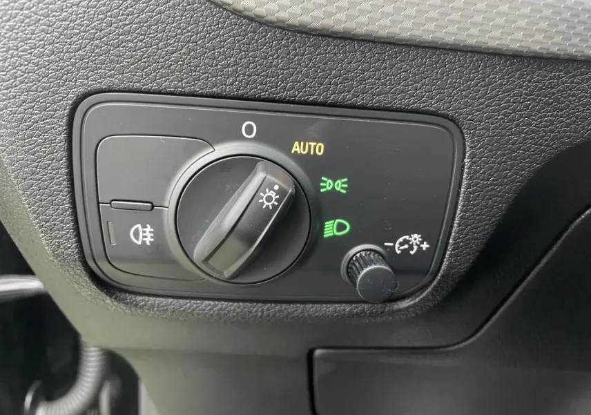 Gros plan sur le bouton de commande des phares avec réglage automatique dans l'Audi Q2 noir Mythic 2023.