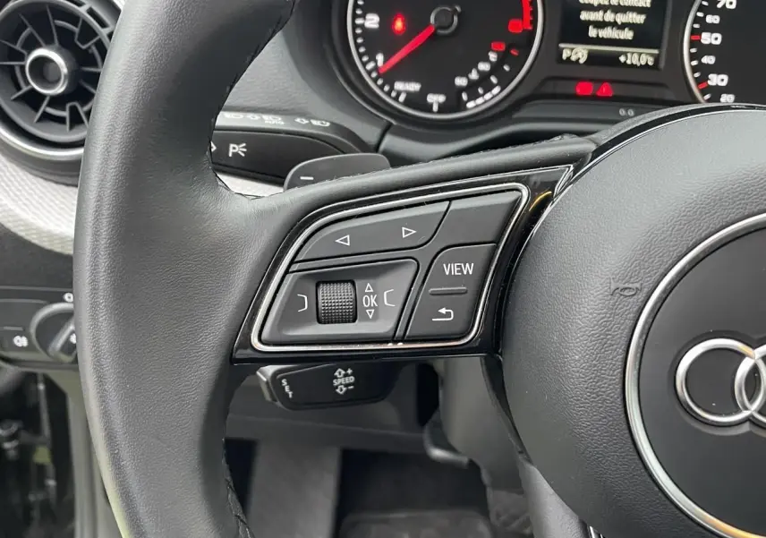 Gros plan sur le volant multifonction noir de l'Audi Q2 35 TFSI 2023 avec commandes intégrées et tableau de bord partiel.