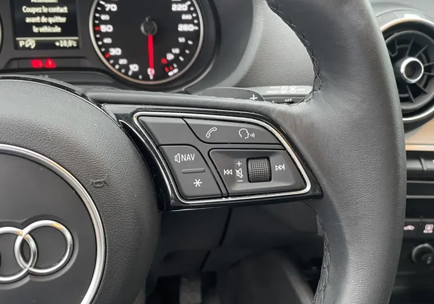 Gros plan sur le volant cuir noir de l'Audi Q2 2023, avec commandes multifonctions et tableau de bord partiel visible.