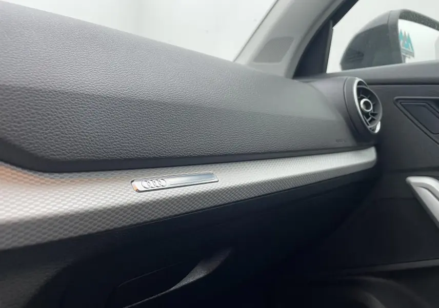 Détail de la planche de bord côté passager de l'Audi Q2 35 TFSI 2023 avec insert décoratif argent et sortie d'air ronde.
