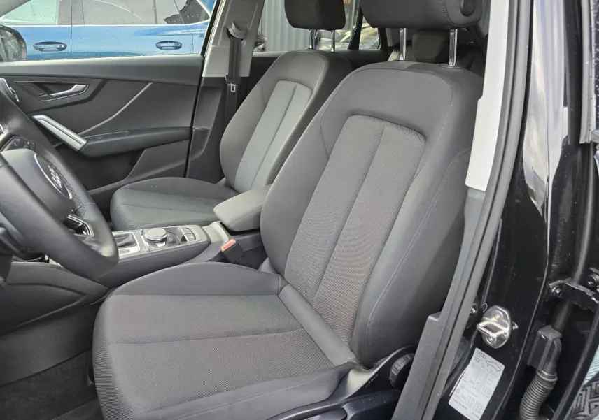 Vue intérieure côté conducteur de l'Audi Q2 35 TFSI noir mythic, montrant les sièges avant en tissu gris et la console centrale.