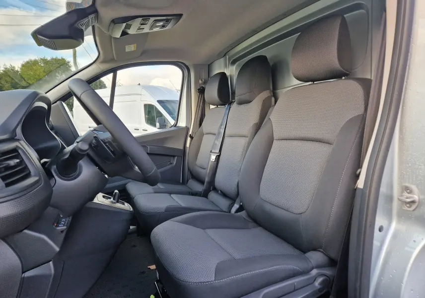 Vue intérieure côté conducteur du Renault Trafic Fourgon gris Highland 2025, montrant les sièges avant et le volant.