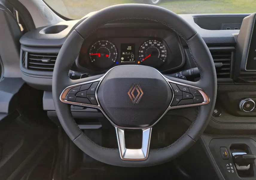 Vue rapprochée du volant noir avec logo Renault du Trafic Fourgon 2025, tableau de bord et commandes visibles.