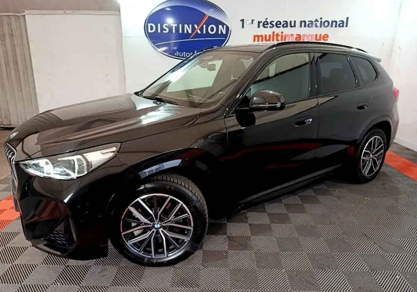 BMW X1 xDrive23i M Sport noir en 3/4 avant droit, avec jantes alliage et phares LED visibles en intérieur showroom