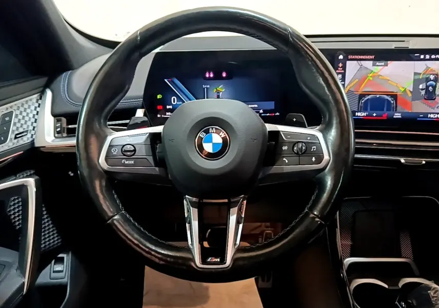 Volant cuir noir BMW X1 xDrive23i M Sport 2023 vu de face avec tableau de bord digital et écran tactile de navigation.