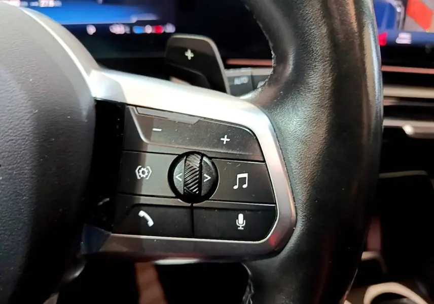 Gros plan sur la partie gauche du volant cuir noir du BMW X1 xDrive23i M Sport 2023 avec commandes audio et vocales.