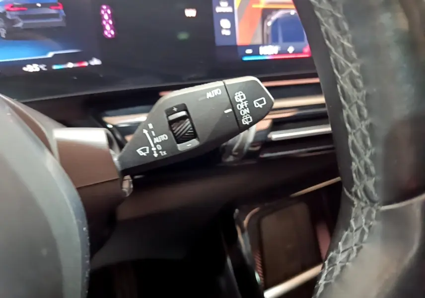 Gros plan sur la commande d’essuie-glace à gauche du volant cuir d’une BMW X1 noire, avec tableau de bord numérique en arrière-plan.