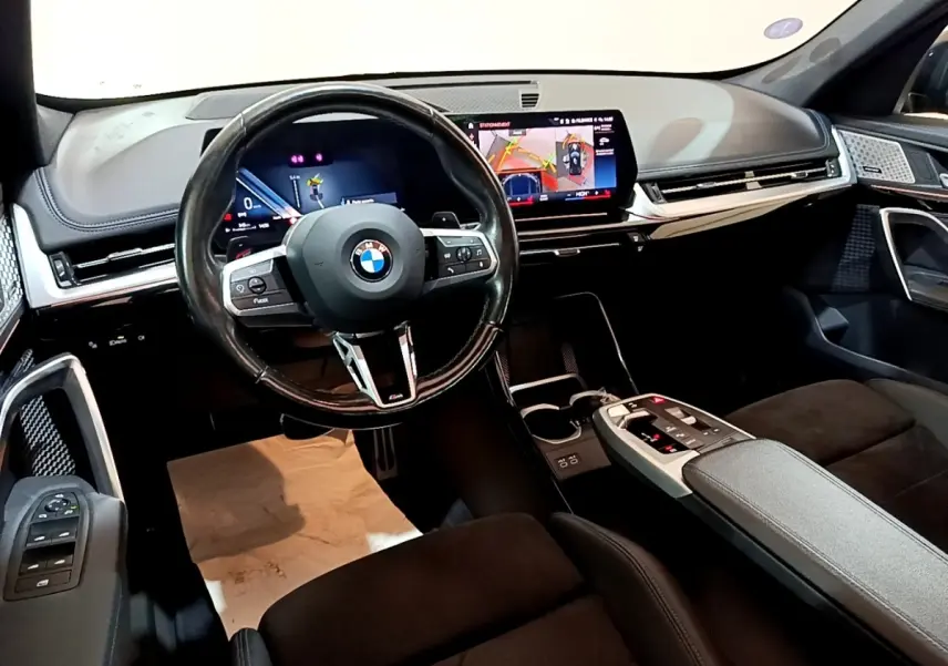 Intérieur noir du BMW X1 xDrive23i M Sport 2023, vue du poste de conduite avec écran tactile et volant cuir multifonctions.