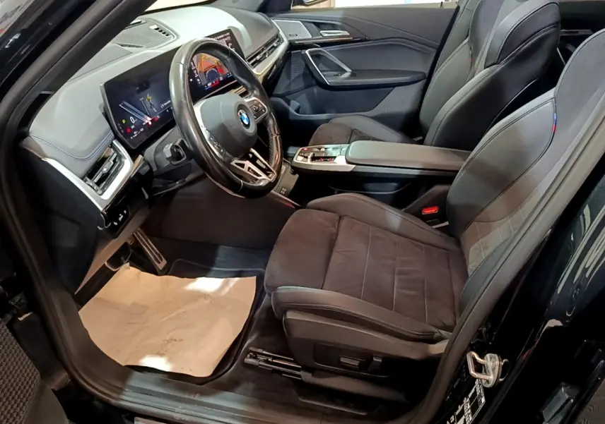 Intérieur noir du BMW X1 xDrive23i M Sport 2023 vu côté conducteur, avec tableau de bord digital et sièges sport.