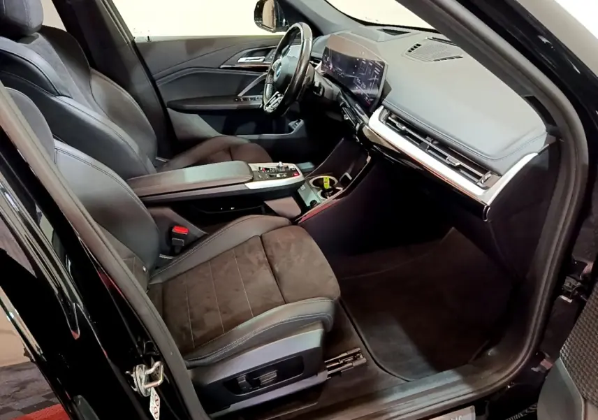 Intérieur noir du BMW X1 xDrive23i M Sport 2023 vu côté conducteur, avec tableau de bord digital et sièges en cuir.