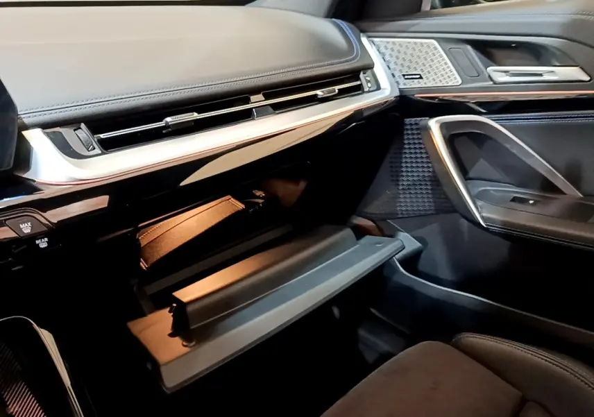 Intérieur BMW X1 xDrive23i M Sport 2023, vue côté passager sur boîte à gants ouverte et garnitures noires élégantes.