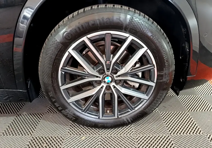 Gros plan sur la roue avant gauche noire d'un BMW X1 xDrive23i M Sport 2023 avec jante alliage distinctive.