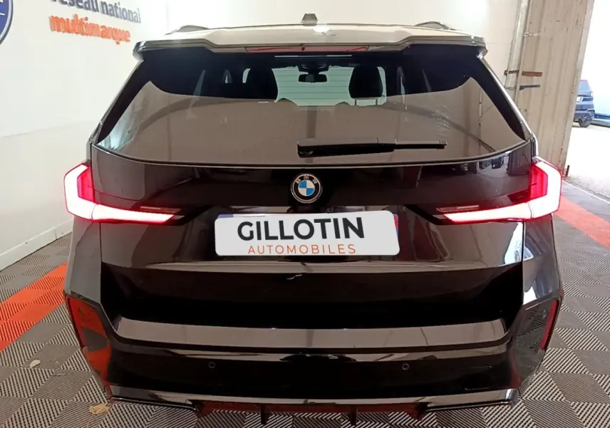 Vue arrière d'un BMW X1 noir 2023 avec feux LED allumés dans un garage intérieur.