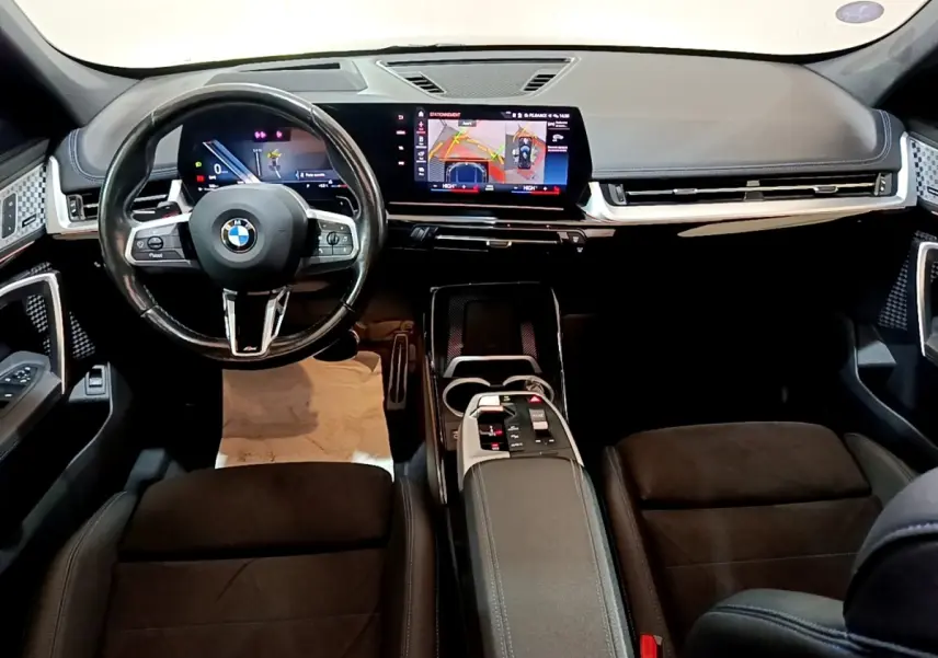 Intérieur noir du BMW X1 xDrive23i M Sport 2023 vu de face, tableau de bord numérique et écran tactile central lumineux.