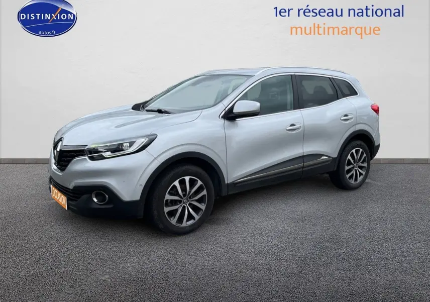 Renault Kadjar gris platine en 3/4 avant droit, avec jantes alliage et barres de toit visibles.