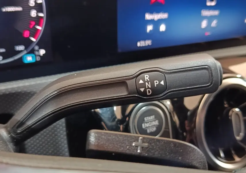 Gros plan sur la commande de boîte automatique noire avec levier de vitesses et bouton start/stop dans un Mercedes Classe A gris clair.