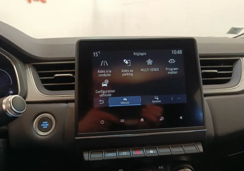 Vue rapprochée de l’écran tactile central et du bouton démarrage du tableau de bord du Renault Captur Intens E-TECH gris clair.