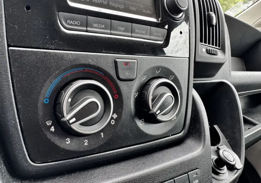 Gros plan sur les commandes de climatisation et radio du tableau de bord noir du Citroën Jumper blanc de 2019.