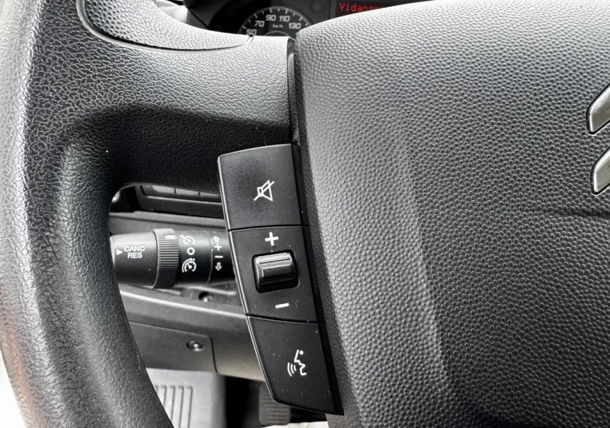 Gros plan sur le volant multifonctions noir du Citroën Jumper blanc, avec commandes de volume et de téléphone visibles.