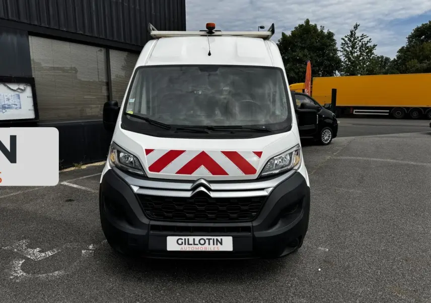 Vue avant d'un Citroën Jumper blanc avec marquage rouge et blanc en chevrons sur le capot, stationné sur un parking.