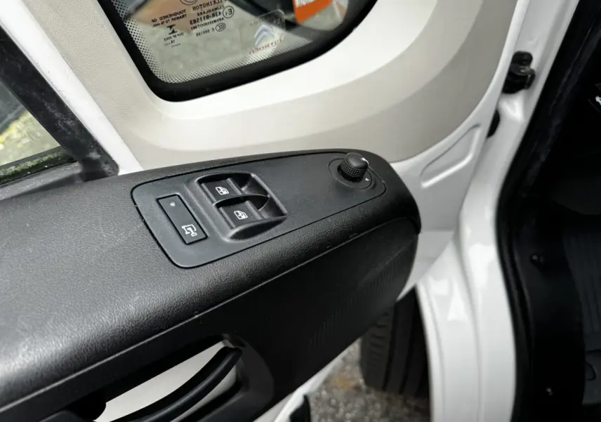 Détail des commandes de lève-vitres et réglage des rétroviseurs sur la porte avant gauche blanche d’un Citroën Jumper 2019.