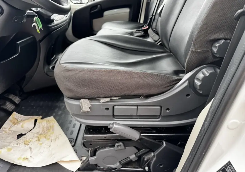 Vue intérieure côté conducteur du siège avant noir usé du Citroën Jumper blanc de 2019 avec levier de frein à main visible.