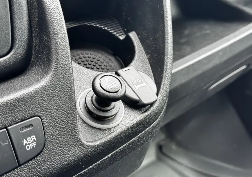 Gros plan intérieur sur la prise 12V et allume-cigare du tableau de bord noir du Citroën Jumper blanc.