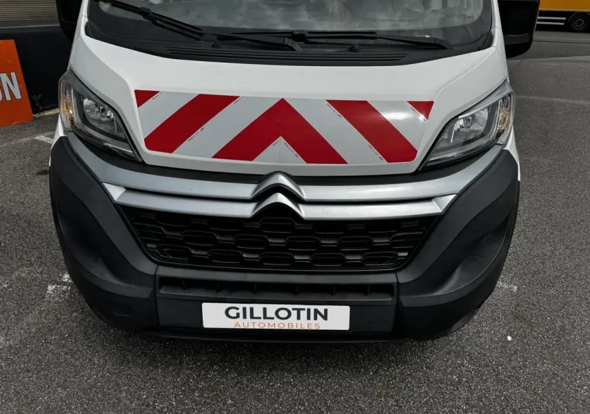 Vue frontale rapprochée du Citroën Jumper blanc avec bandes rouges réfléchissantes sur le capot et calandre noire.