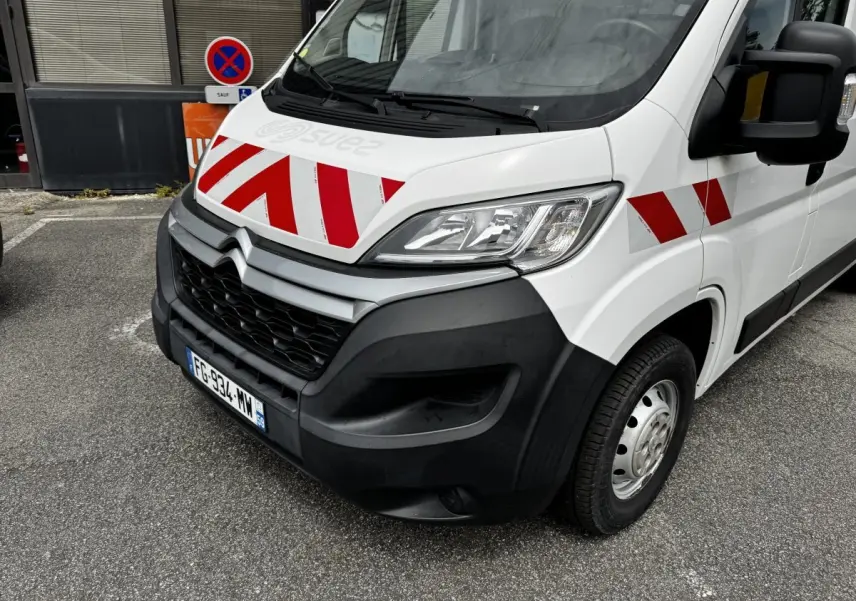 Vue 3/4 avant droit d’un Citroën Jumper blanc avec bandes rouges diagonales sur le capot et l’aile.