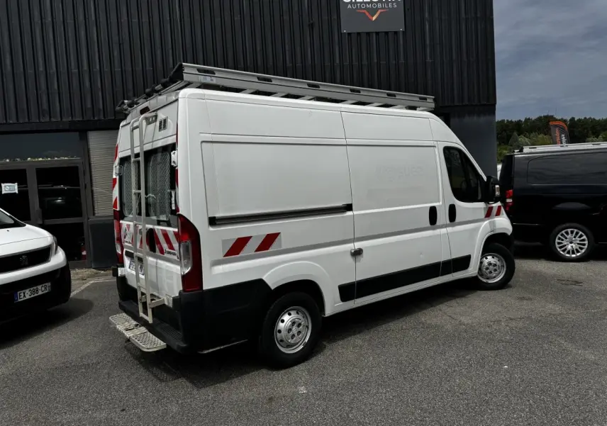 Vue 3/4 arrière droite d’un utilitaire Citroën Jumper blanc avec marquages rouges et échelle sur porte arrière.